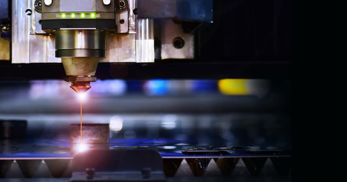 A laser marking machine aims a focused beam of orange light at a metal material in an industrial setting.