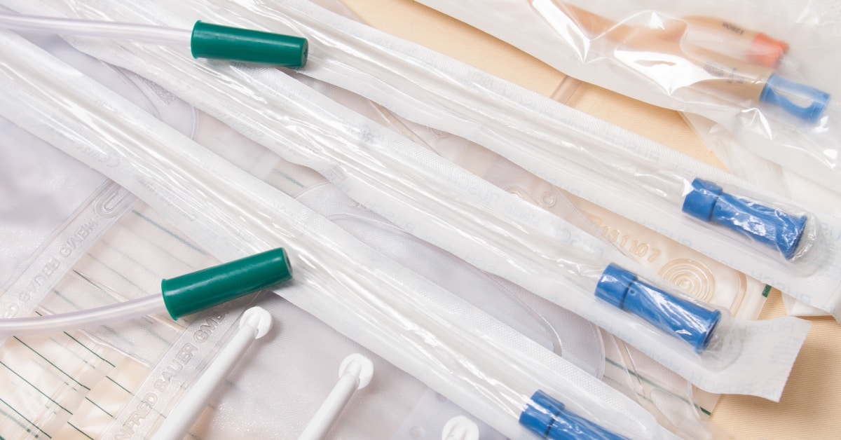 Multiple blue and green catheters displayed on a wooden table in their white, transparent, plastic packaging.