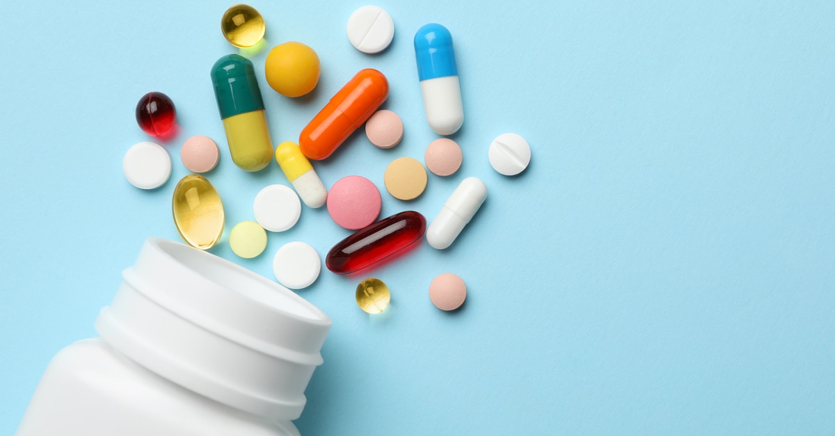 An overhead view of medicinal pills and tablets of various shapes and colors on a blue background next to an open bottle.