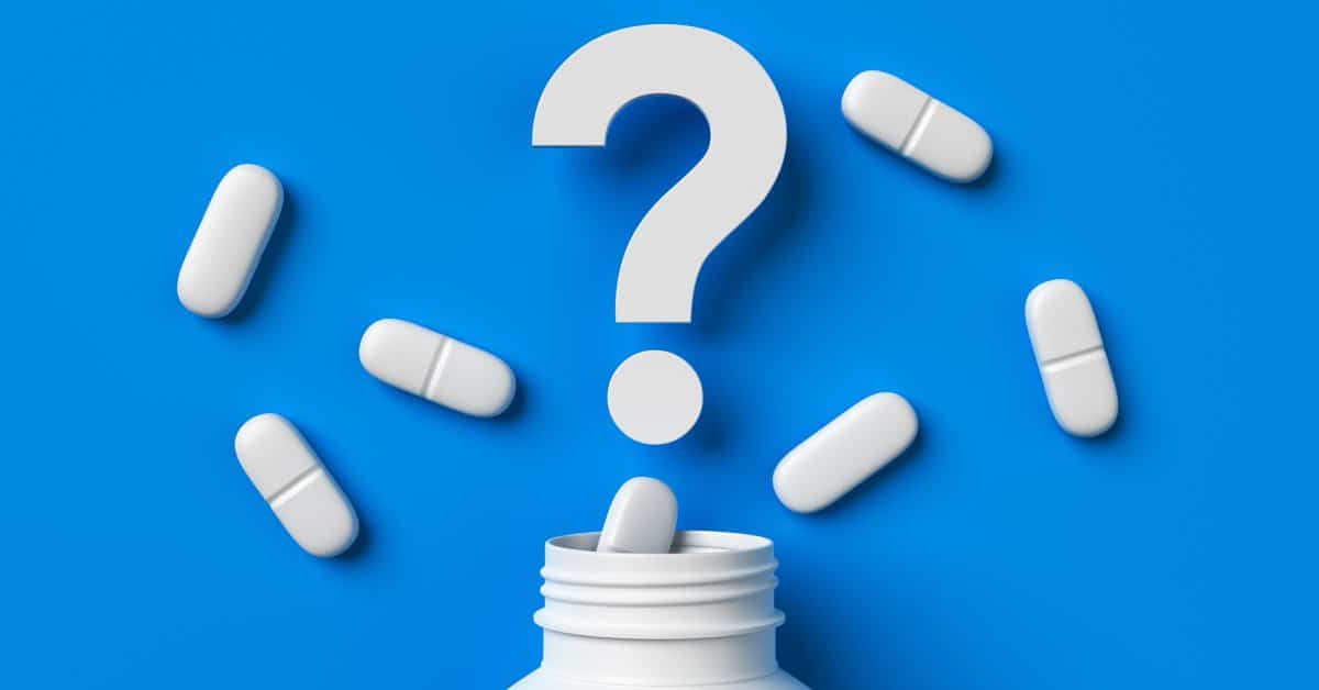 The top of a pharmaceutical bottle opened with various pills laid out around a large question mark over a blue background.