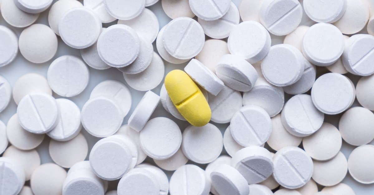 A pile of white, rounded pharmaceutical tablets with one yellow, oval pill in the center of the pile.