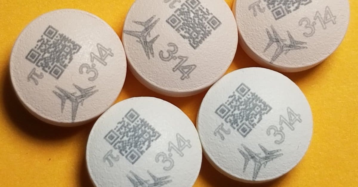 A close-up of three oral medication tablets with various markings printed on them, including the Pi symbol and a QR code.
