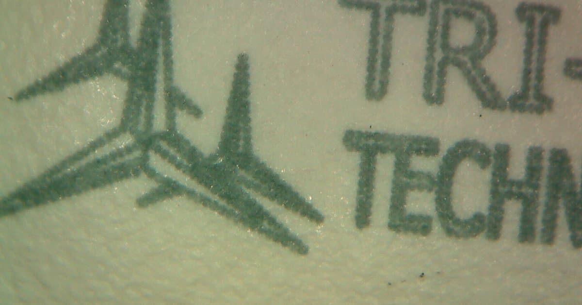 An extreme close-up of the surface of an oral medication tablet with the Tri-Star Technologies logo printed on it.