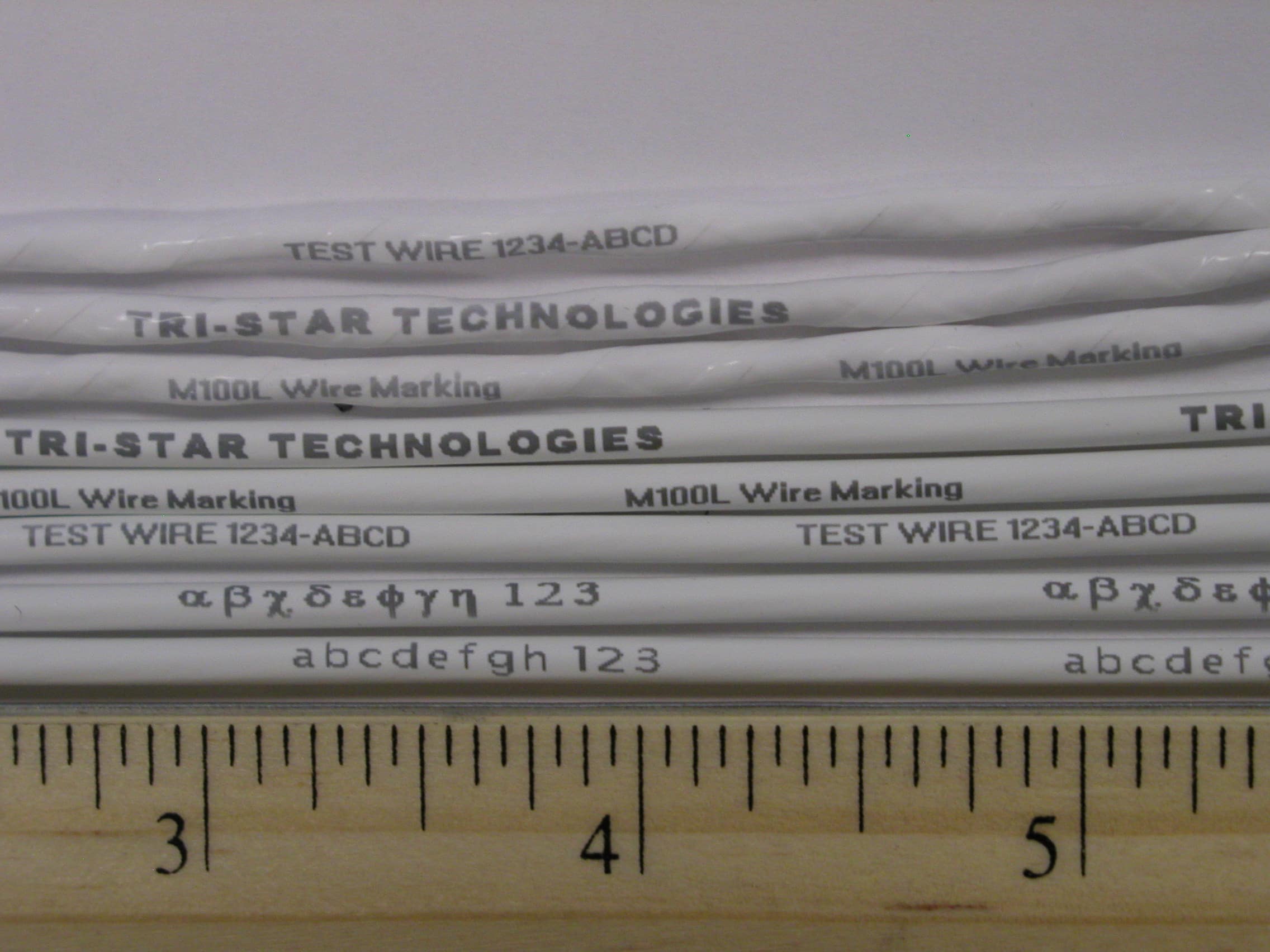 A close-up of white insulated wires with test sample markings in various fonts and sizes from Tri-Star's laser markers.