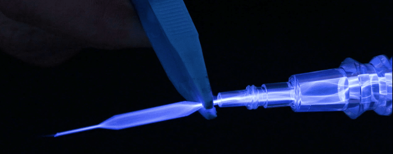 A close-up of a pair of pliers grabbing onto the end of a catheter as it glows blue and white from plasma treatment.