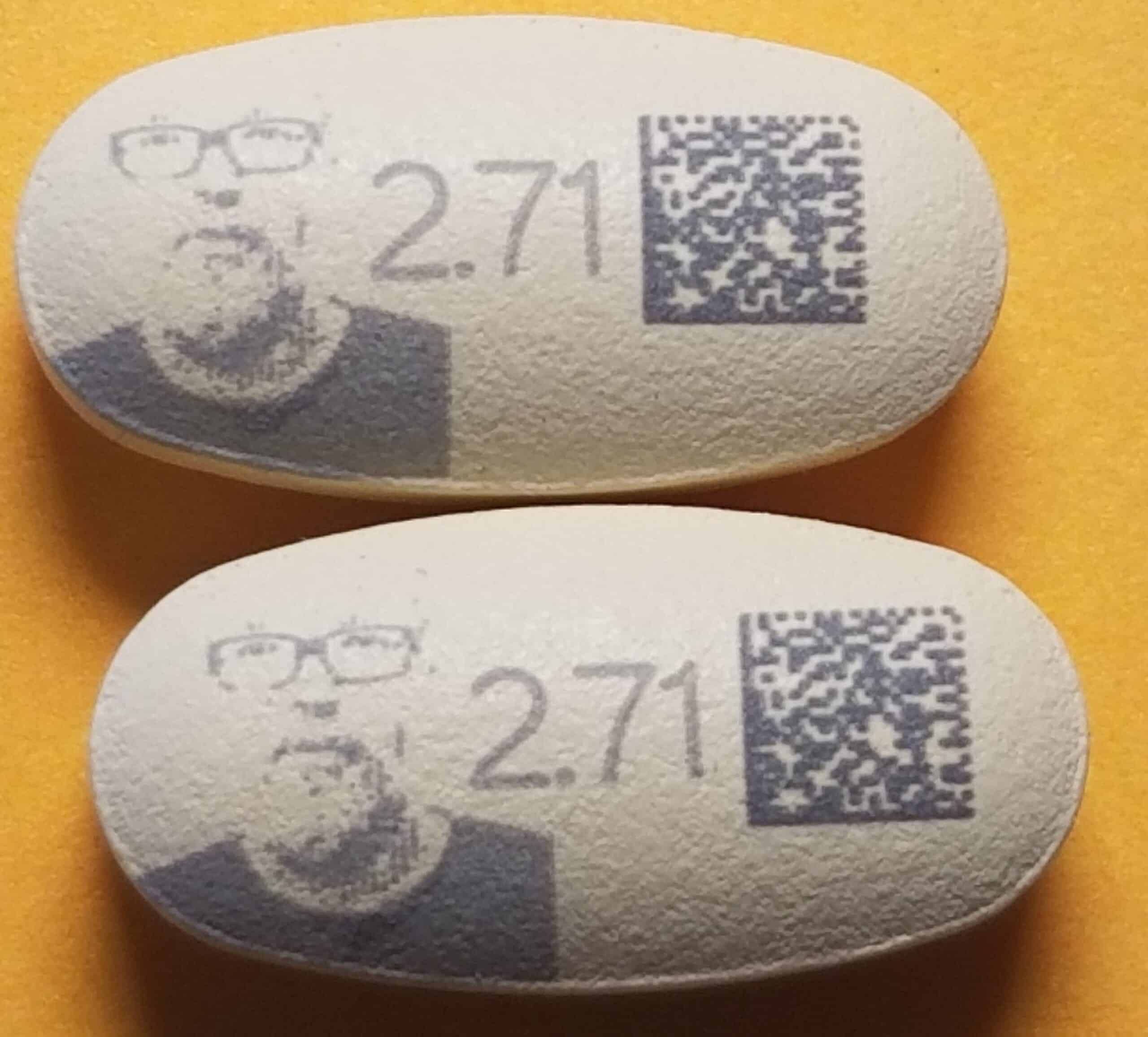 A close-up of two oval prescription medicinal tablets with a QR code, three numbers, and a man's face printed on them.