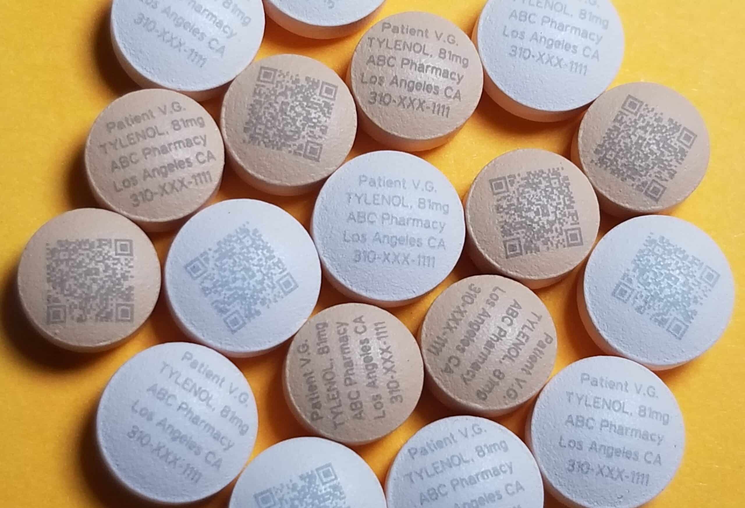 A close-up of various round medicinal tablets with printings on them, including QR codes and drug information.