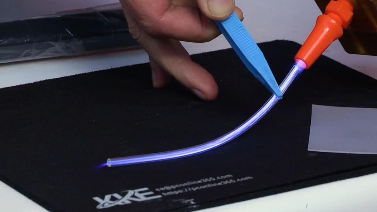 A close-up of a hand using pliers to hold up a small plastic tube to the DURADYNE atmosphere plasma cleaning system.